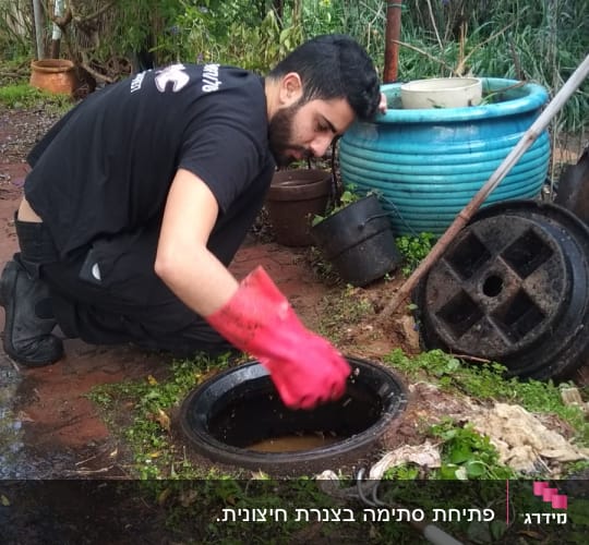 אדם עם כפפות אדומות מנקה ביוב בחצר